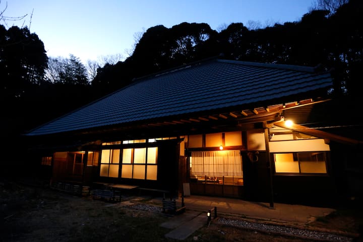 夕暮れに灯りがともる茅葺き屋根の風格ある古民家
