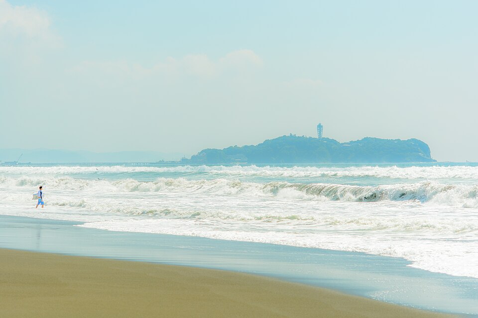 片瀬海岸から望む江の島。波打ち際をサーファーが歩く